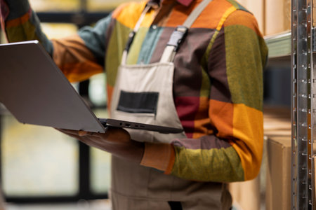 Close up of black male overseeing order processing and products stock on laptop, ensuring parcels are prepared correctly for shipment. Small delivery services for e-business operations.の写真素材