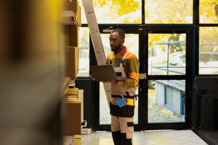 Black staff member organizing product retail inventory in a small depot, preparing cardboard boxes for e-business shipments and supporting express delivery with transportation logistics.の写真素材