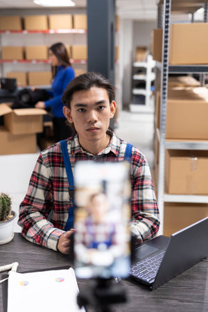 Small business owner uses a smartphone to film content inside fulfillment center, vlog highlighting inventory, order processing and local delivery services for regional online promotion.の写真素材