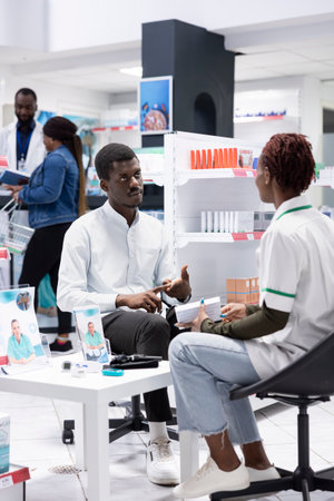 Black pharmacist discussing pharmaceutical care and prescription drugs with a client at the pharmacy dispensary, offering expert advice on the proper use of capsules and medication dosage.の写真素材