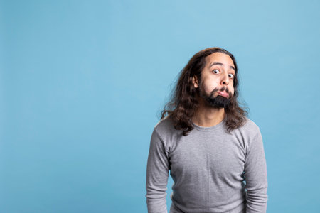 Joyful bearded man with long curly hair strikes a silly pose showing a carefree attitude. Playful...