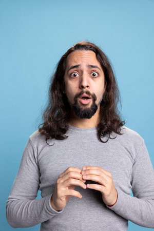 Amazed surprised young adult with long curly hair in studio acting excited and astonished about...