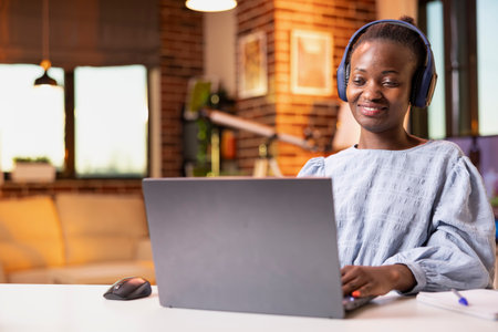 Smiling woman with headphones reading online articles and checking business contracts on laptop....