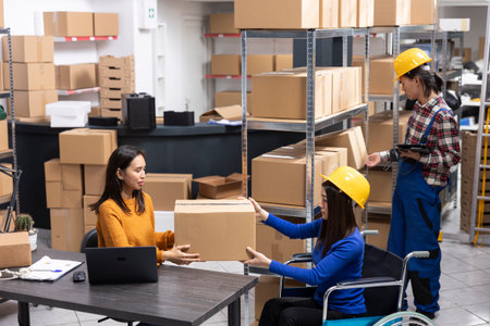 Woman in wheelchair working in a retail distribution hub, managing goods and express delivery. Inclusive space supporting local delivery with logistics and product handling stations.の写真素材