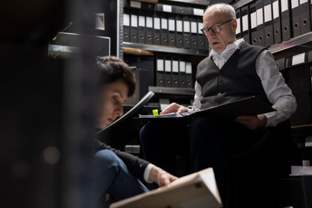 Commissioner and woman agent conduct background check in evidence room, studying case files and comparing fingerprints. Tracing connections between criminal suspects and illegal activity.の写真素材