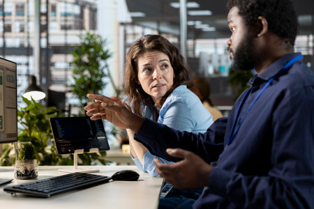 Manager reviews company infographics with a team member in a corporate office, making important...