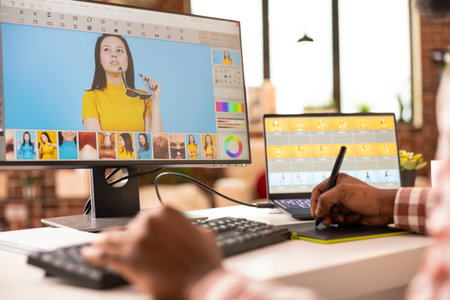 Creative freelancer using stylus and color editing software to adjust portrait photos on dual monitors. Closeup of african american photographer retouching images on computer for his portfolio.の写真素材