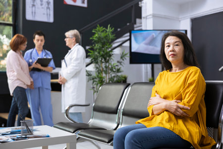 Portrait of a mature asian woman arriving early at the clinic for examination, sitting in the waiting area and preparing for general routine checkup with physician. Healthy lifestyle.の写真素材