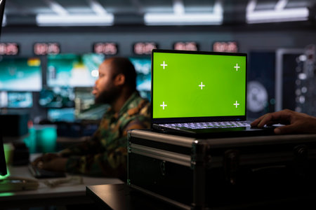 Combat specialist working on green screen laptop in surveillance monitoring center filled with...
