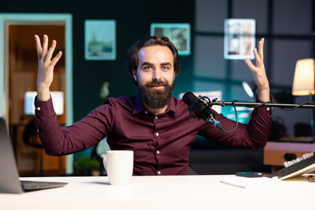 Joyful internet star shooting video, doing frantic gesturing in studio. Jovial man making hectic hand movements while filming vlog with professional microphone and cameraの写真素材