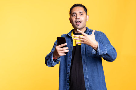 Portrait of a stylish Indian man with satisfied facial expression using his mobile phone, reading good news pleased in studio. Scrolling through social media apps connected to the internet.の写真素材