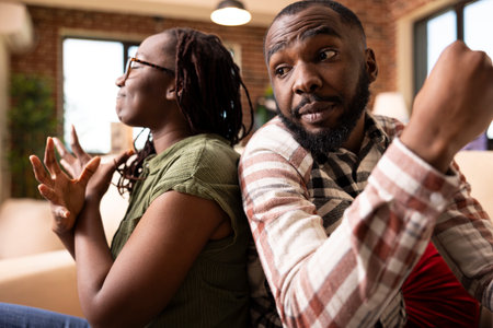 Black couple facing relationship conflict at home. African american woman looks disheartened with eyes closed while boyfriend speaks with expressive gestures during tough conversation.の写真素材