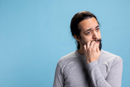 Middle eastern man biting his nails in studio, having a nervous tic and being worried about...