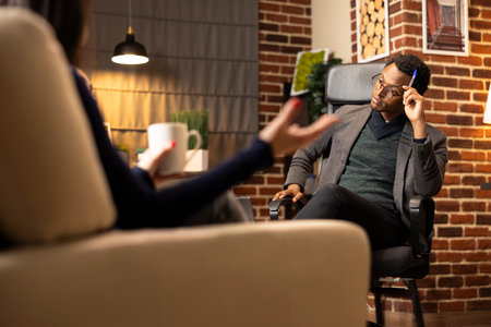 Black male psychiatrist holds pen to forehead, trying to focus on clients sharing relationship...