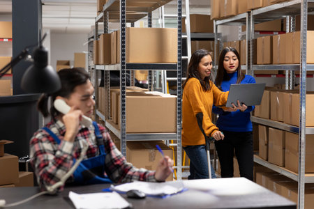 Asian woman on crutches works in a supply room shipping area, helping manage orders packages and...