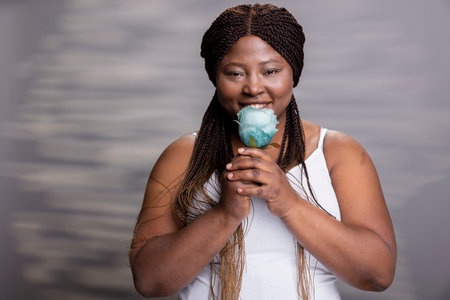 African american female holding a beautiful blue rose for cosmetics ad, promoting self love and body...