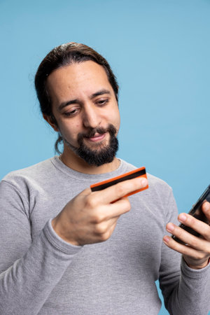 Pleased cheerful guy entering his credit card details on a website, feeling happy doing online...