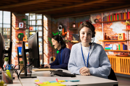 Portrait of smiling call center employee wearing headset speaking into microphone. Happy customer...