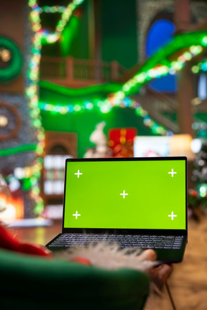 Person dressed as Santa Claus using chroma key laptop to read letters from kids. Man portraying Father Christmas answering emails received from children using isolated screen notebookの写真素材