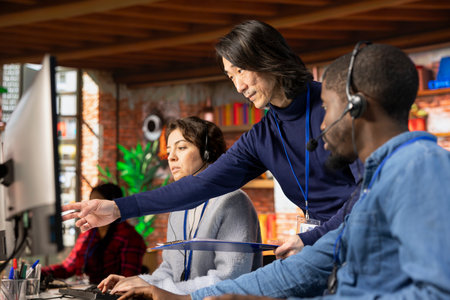 Asian call center manager providing guidance to multiethnic team, addressing questions. Customer...