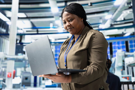 Female tech specialist reviewing assembly line insight on laptop, manages factory activity in a solar panel plant to ensure effective quality control and commitment for renewable energy.の写真素材