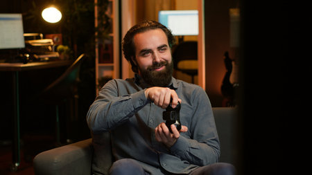 Joyful gamer at home gaming and enjoying leisure time. Smiling man sitting on couch in neon lit...