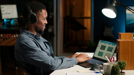 Financial manager doing remote accounting work with music on headset, solving his tasks on laptop at...