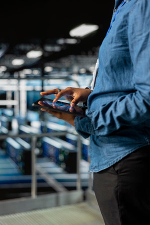 Close up of black admin using tablet to do infrastructure AI machine learning automatization in server farm, doing maintenance using neural network systems. Data center software developer.の写真素材