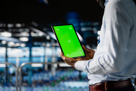 Male technician overseeing neural network using chroma key on tablet, reviewing LLM visualization. Server farm IT expert oversee rigs powering machine learning processes, industrial platform.の写真素材