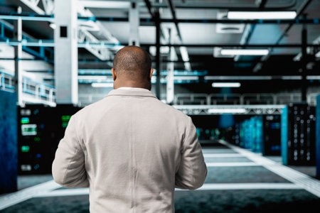 Engineer doing yearly checkup to prolong data center hardware life span and avoid downtime. African american employee in server room monitoring server infrastructure componentsの写真素材