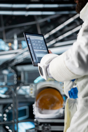 Close up of astronaut reviewing spacecraft diagnostics on tablet to ensure safe operation during space travel. Crew member monitors system stability while preparing for next phase of cosmic journeyの写真素材