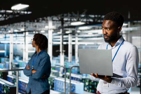 Smiling black technician and colleague in data center reviewing large language model visualizations on PC. Professional IT engineering team analyzing neural network performance outputs.の写真素材