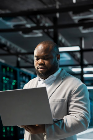 Data center engineer using laptop, monitoring and analyzing metrics to enhance operational...