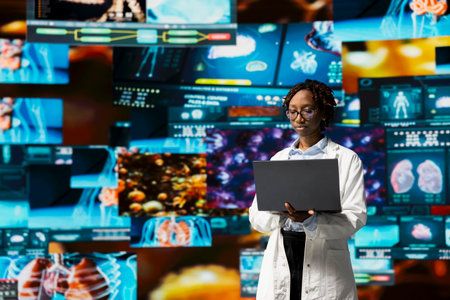 Doctor in lab coat monitoring medical research data and 3D anatomy models dashboards with laptop...