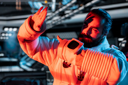 Astronaut in spaceship raises hand defensively as unidentified alien threat triggers onboard alert. Crew member reacts to red light warning coming from extraterrestrial form disturbanceの写真素材
