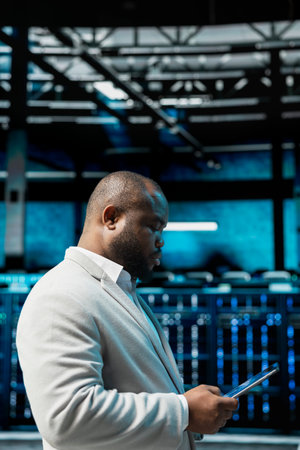 Server hub admin checking recovery plan on tablet, tracking resource utilization trends. Data center IT expert scanning hardware logs for faults, making sure rigs are functioning optimallyの写真素材