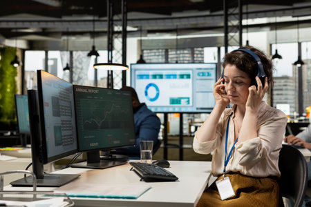 Woman employee in corporate office works with music on headset, developing a new business strategy...