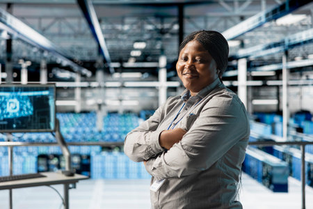 Portrait of smiling data center technician tasked with reviewing code for AI automation scripts. Happy african american woman in server hub running artificial intelligence assisted diagnostics on gearの写真素材