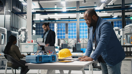 African american industrial expert inspecting solar panels production with models on papers, reading important insight to guarantee sustainability and renewable power, modern factory. Camera A.の写真素材