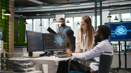 Junior dev and coworker in wheelchair developing software applications, optimizing code. Female technician and colleague with paraplegia in office using AI to solve bottlenecks, camera Aの写真素材