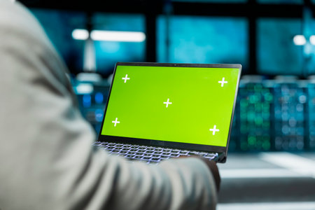 Close up of programmer in data center using green screen laptop to check for server performance issues. IT professional in server hub fixing errors slowing down hardware using mockup notebookの写真素材