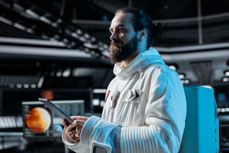 Cosmonaut in orbital station looking at Mars data analysis interface on tablet. Man working on orbital station looking at galaxy visualization, doing Martian surface research to assist planetary explorationの写真素材