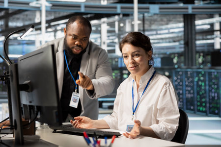 Data center manager supervising work done by engineer updating servers tech, configuring gear using...