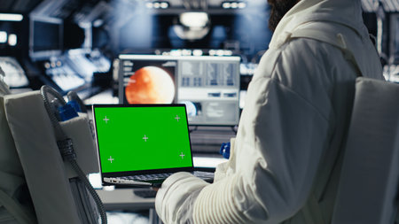 Astronauts reviewing onboard analytics on isolated screen laptop before stepping outside starship. Cosmonauts verifying parameters on chroma key notebook after landing on planetの写真素材