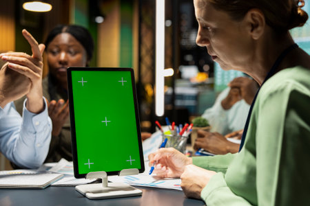 Diverse project staff working at night in office with chroma key on tablet, collaborating on...