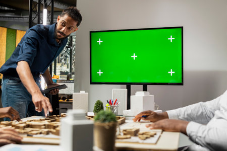 Property engineers team study architectural blueprints with a mockup on TV, collaborating in a smart city urban development master plan. Modern residential project with infrastructure goals.の写真素材