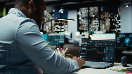 African american consultant examining data on stock and forex trading, preparing reports and...