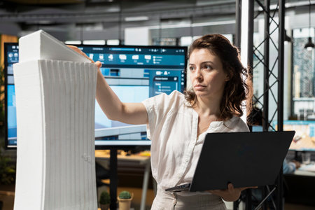 Female contractor in real estate reviews 3D construction models in an office, city planning for a new building project in residential redevelopment. Modern housing for urban development.の写真素材