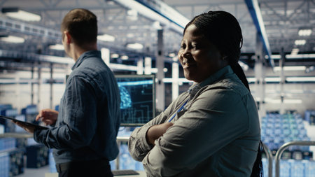 Portrait of smiling data center manager working to improve AI rigs processing speed and efficiency. Happy team leader in server hub manages gear to support artificial intelligence workloads, camera Bの写真素材