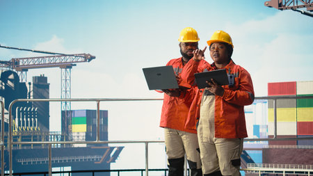 Offshore platform colleagues supervising deck operations with devices, ensuring compliance with...